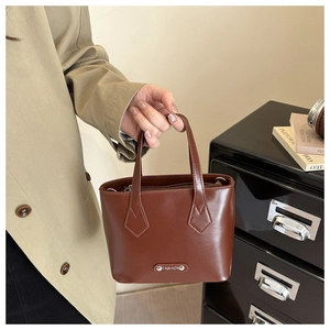 Close-up of brown PU leather handbag featuring a metal plate and dual top handles