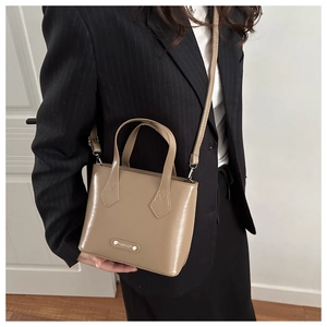 Detail of khaki leather bucket bag with metal logo tag worn with a black blazer suit