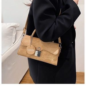 Detail of khaki suede crossbody bag with wave flap and silver chain lock on black blazer