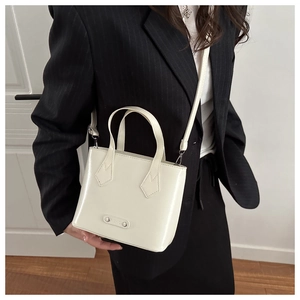 Detail of cream mini bucket bag in glossy patent leather with fashion metal plaque