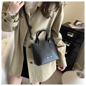 Detail of black leather trapezoid tote bag with FASHION metal plaque and thin shoulder strap