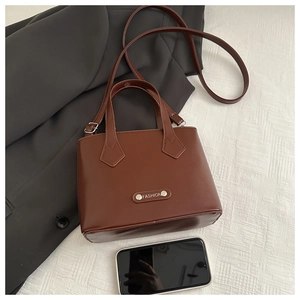 Top view of brown PU leather tote bag with metal label next to a smartphone