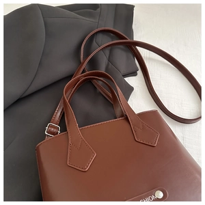 Detail view of dark brown leather handbag with silver metal buckle on black suit