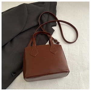 Detail of vintage brown leather handbag with adjustable strap on gray blazer background