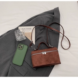 Detail einer braunen Umhängetasche aus Wildleder auf einem grauen Blazer mit Dekoration