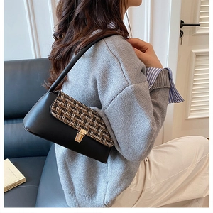 Detail of tweed flap handbag with gold metal clasp on a stylish black leather underarm bag