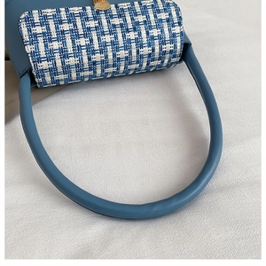 Detail of blue and white tweed woven shoulder bag with elegant gold metal clasp and leather handle