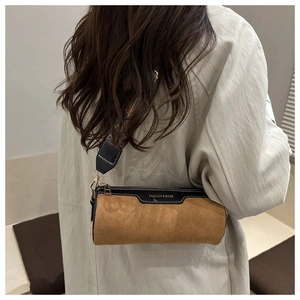 Detail of cylinder crossbody bag with brown suede finish and colorful woven shoulder strap