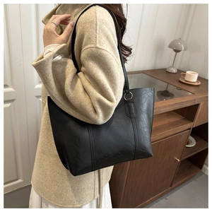 Detailed view of black minimalist tote bag with gold metal rings on leather handle