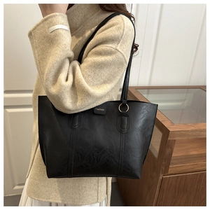 Close-up of black leather tote bag featuring golden Fashion logo and metal ring detail