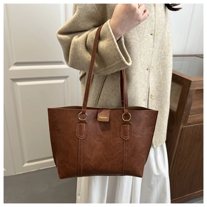 Close-up of brown wax leather texture and gold-tone Fashoin logo on a large tote bag