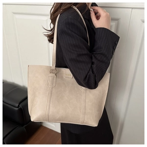Detail of beige tote bag with long straps and Fashion metal logo in a lifestyle shot