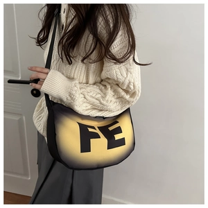 Détail du sac bandoulière demi-lune avec dégradé jaune et imprimé FE sur pull blanc