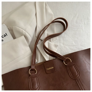 Detail of dark brown pebble leather tote bag with gold rings and Fashion label