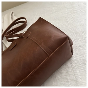 Detailed shot of dark brown tote bag showing textured PU leather and fashion tag