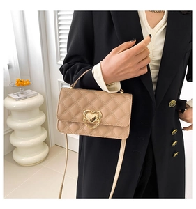 Detail of beige quilted crossbody bag with golden heart-shaped metal lock and chain