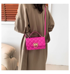 Detail of rose pink quilted crossbody bag with golden heart buckle on a tan coat