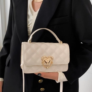 Chic cream-colored quilted crossbody bag with heart lock and chain on a black blazer