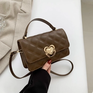 Brown quilted crossbody bag with gold heart buckle held by a model in a blazer