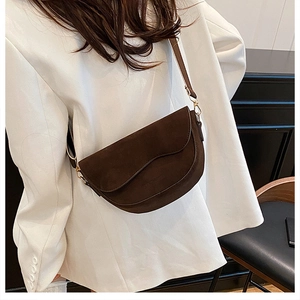 Gros plan d'un sac besace marron foncé en daim avec bordure ondulée et boucles dorées