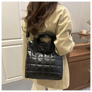 Rear view of a black quilted bucket bag with adjustable nylon shoulder strap on a model