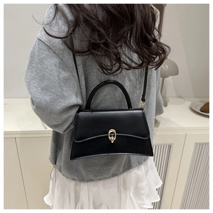 Detail of a chic black trapezoid leather handbag featuring a stylish gold oval metal lock