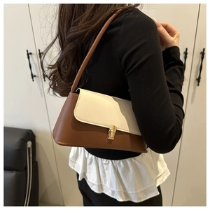 Detail of two-tone leather underarm bag with gold metal buckle shown on shoulder