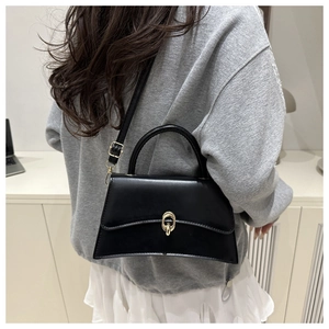 Detail of a minimalist black trapezoid handbag with gold double-ring lock and adjustable strap