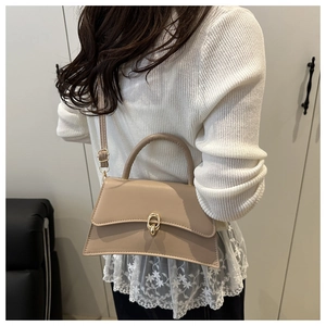 Side view of a beige crossbody bag with gold clasp and curved bottom on model