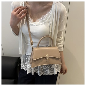 Detail of khaki crossbody bag with curved base and gold lock on white lace outfit