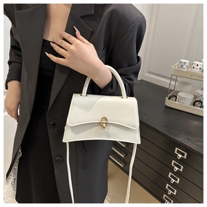 Detailed view of white crossbody bag with gold buckle and curved base on a model