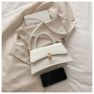 Close-up of a white leather trapezoid handbag with a golden twist lock on a beige blazer