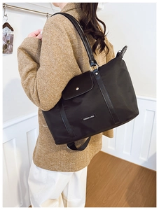 Detail of black tote bag with leather flap pocket and metal buckle in modern interior
