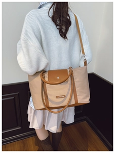 Model wearing a large beige nylon tote bag with brown leather handles and silver buckle
