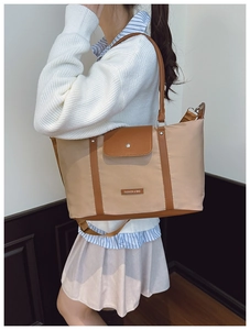 Detail of nylon tote bag featuring brown leather trim and metal fashion logo branding