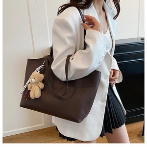 Detail of dark brown leather tote bag with plush bear charm and patterned silk scarf
