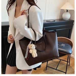 Macro shot of dark brown leather tote bag detailing golden logo and cute bear charm