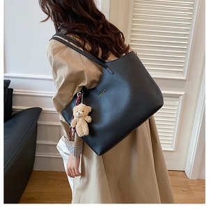 Detail of black large tote bag with bear charm and golden text on beige trench coat