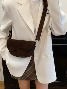 Sacoche selle marron foncé avec large bandoulière portée sur un blazer blanc chic