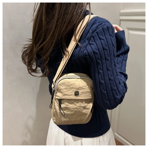 Beige nylon crossbody bag with wide shoulder strap shown on a model from a side view
