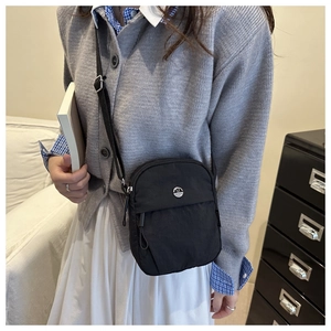 Close-up of minimalist black nylon crossbody bag with dual zippers and adjustable strap
