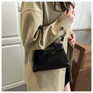 Detail of black quilted leather shoulder bag with top handle worn on a beige trench coat
