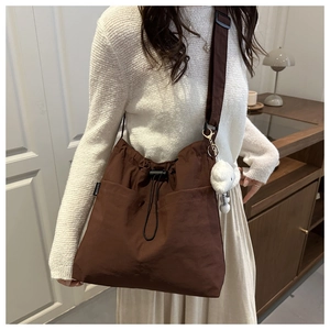 Detail of a brown nylon tote bag featuring side pockets and a white teddy bear charm