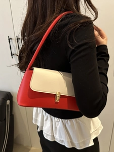 Sac bandoulière en cuir rouge et crème avec boucle dorée porté par un mannequin