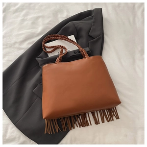 Detailed view of brown tote bag featuring long fringe trim and woven handles on a suit jacket