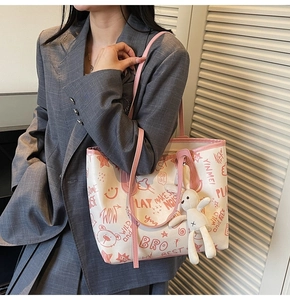 Detail of cute tote bag with pink graffiti prints and a plush bunny charm on a model