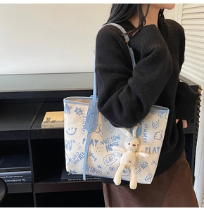 Detail of the doodle print canvas tote bag with light blue handles and bunny charm accessory