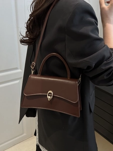 Dark brown leather handbag with gold lock buckle shown on a model in casual attire