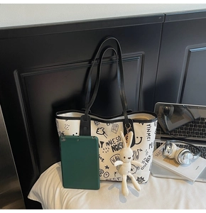 Close-up of white tote bag with black graffiti patterns and a cute plush bunny charm