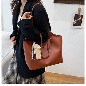 Brown leather tote bag with a cute teddy bear charm and ribbon, worn with a black suit